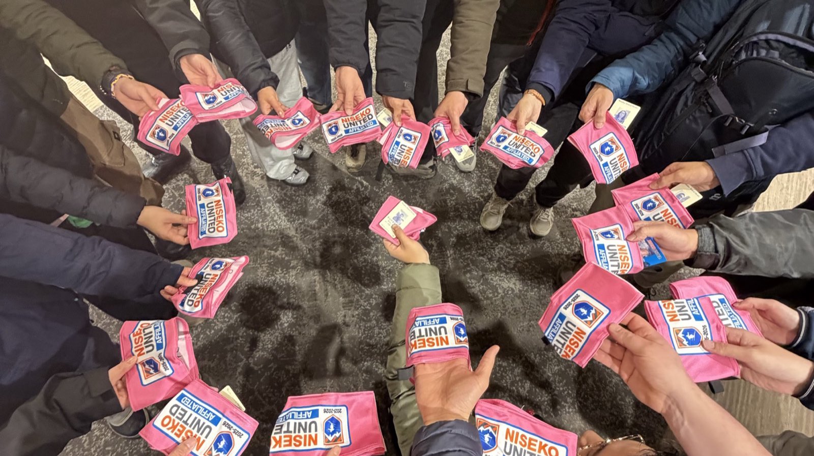 Pinnacle 教練圍成一圈，每人手上舉著自己的 NISEKO UNITED AFFILIATED 認定臂章——Niseko United 官方認定滑雪學校的識別，二世谷雪場規定只有認定學校的教練才能在山上帶課，每位教練上山都戴著